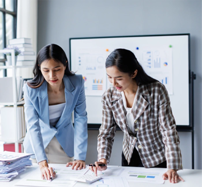 Two businesswomen analyzing financial data and working with documents and a calculator, representing accounting services for businesses.