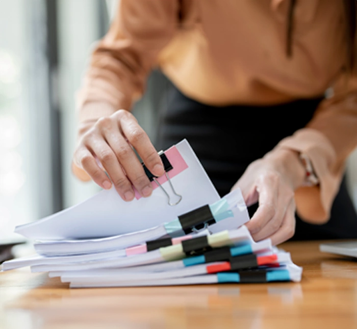 Person organizing stacks of financial documents with color-coded binder clips on a desk, representing professional bookkeeping services.