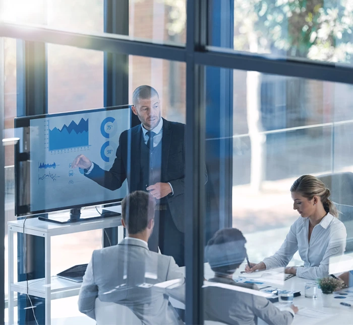 Business professional giving a financial presentation to colleagues in a modern office, discussing charts and graphs on a screen, representing fractional CFO services for businesses.