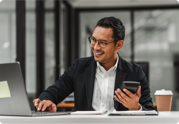 Smiling business professional using a laptop and holding a calculator at a desk, representing excitement about special offers for bookkeeping and financial services.