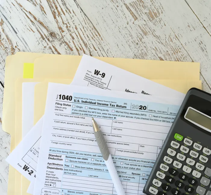 Tax documents, including a 1040 form and W-9, placed on a desk with a calculator and pen, representing tax preparation services for businesses.